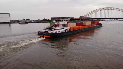 barcaza con contenedores de carga navegando en el río oude maas hasta el puente de arco