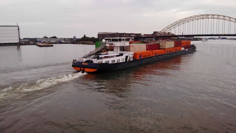 barge with cargo containers sailing in the oude maas river to arch bridge