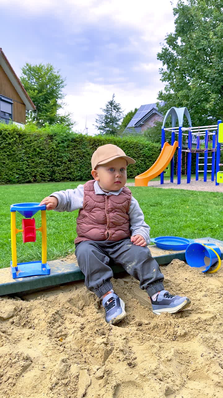 Young boy enjoying a sunny day at the playground while playing in the sandbox with colorful toys and nearby slides