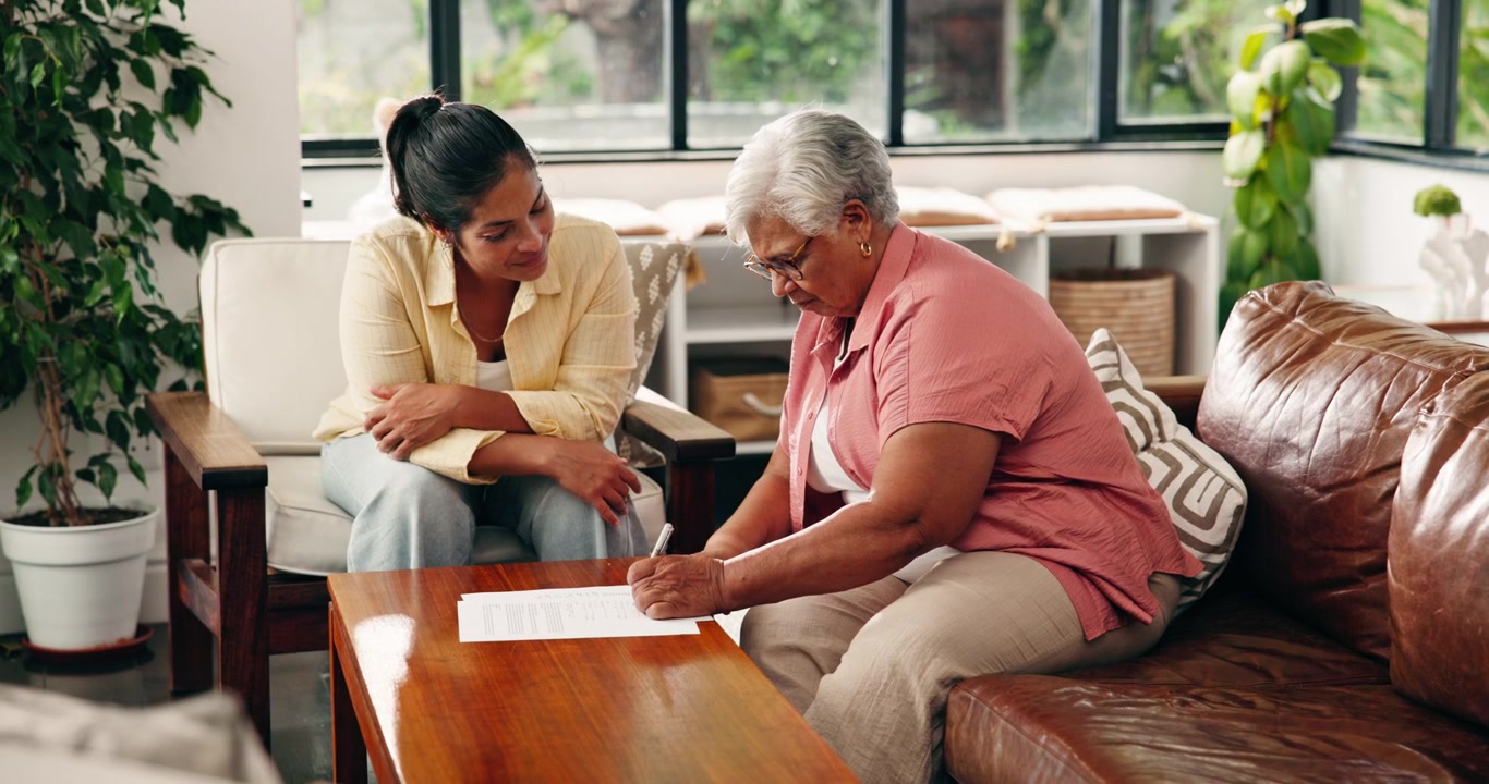 Young Woman Helping Senior Woman Sign Documents at Home