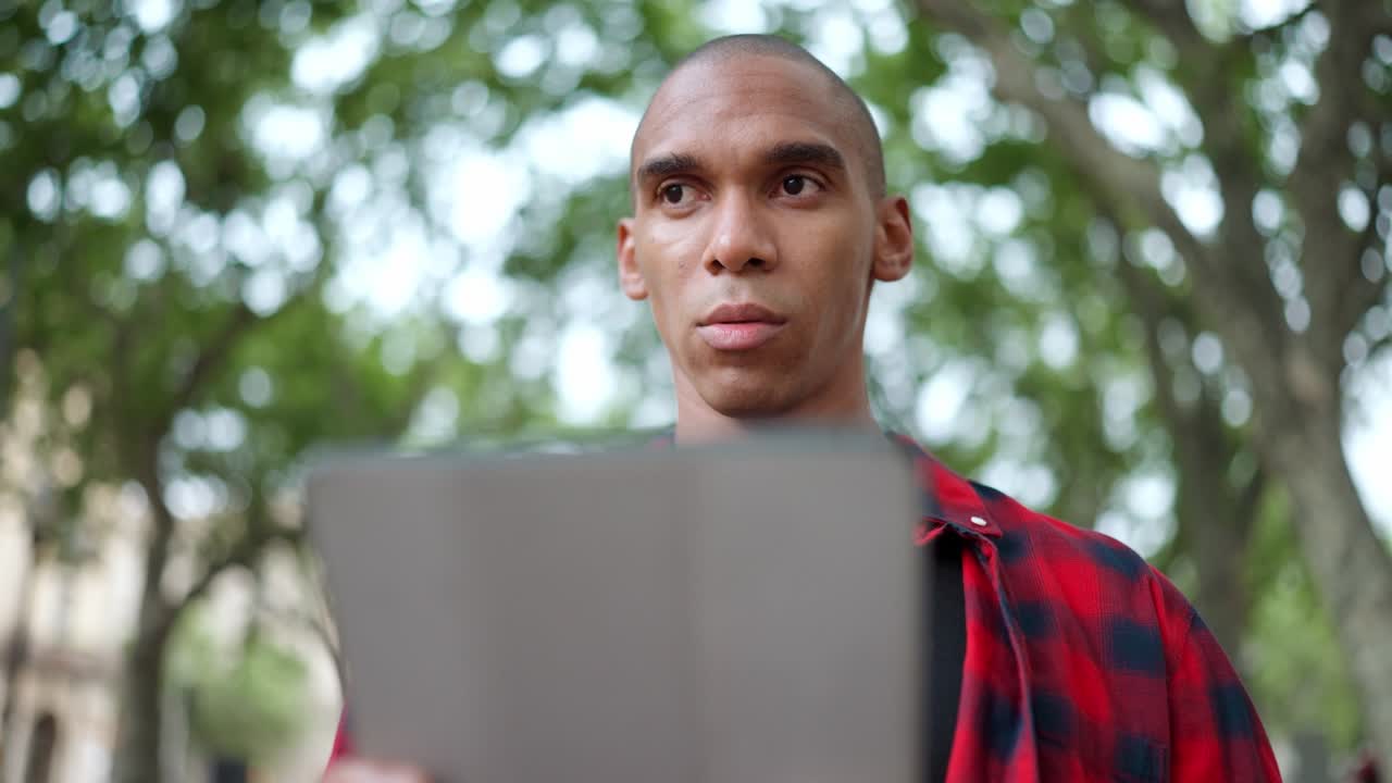 Pensive bald African man typing on digital tablet on bench