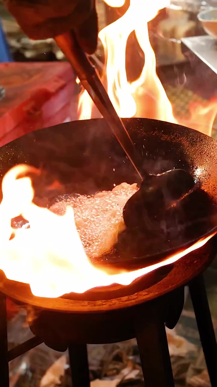 Kok rører energisk i kød i en flammende wok på et natligt street food-marked, dramatisk belysning, håndholdt.
