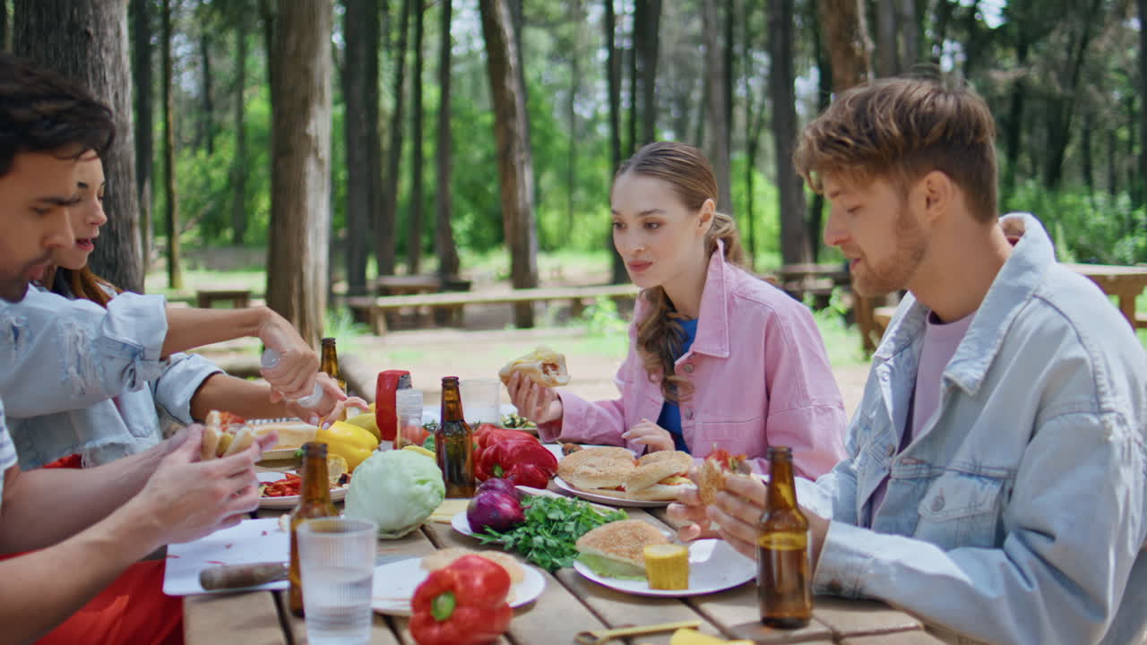 Laughing group eating picnic table in summer forest closeup. Relaxed youngsters