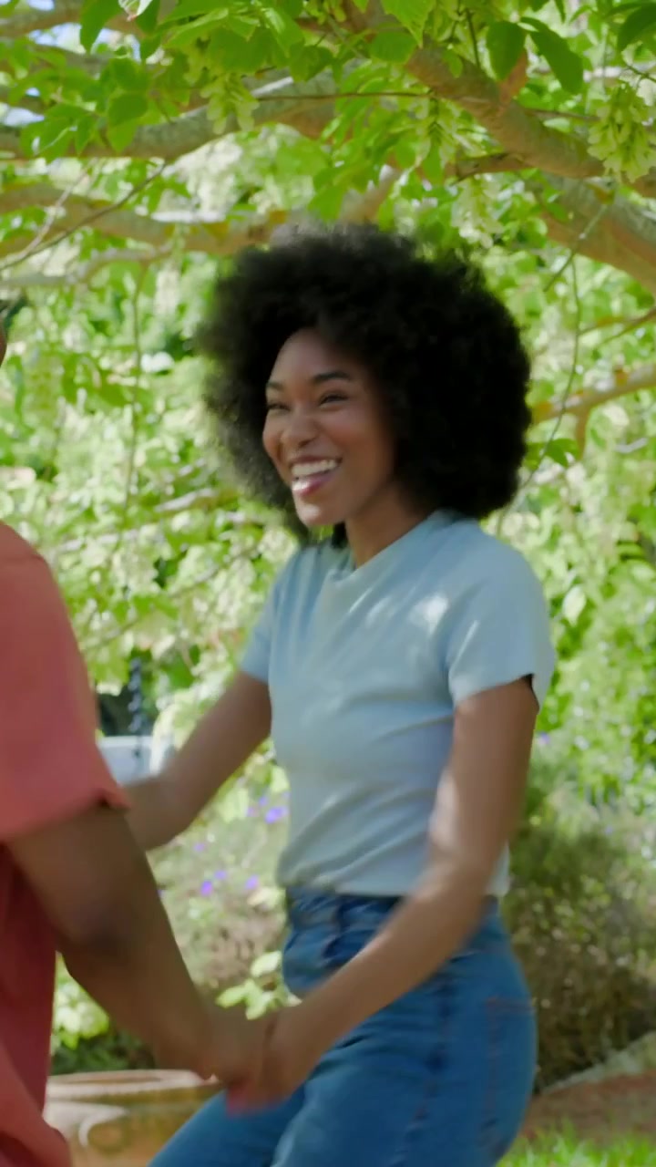 Vertical video: Entering woman reaching for man under tree, sparking playful spin, coral, blue tees