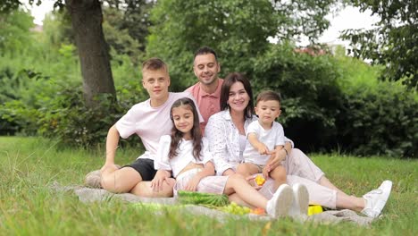 Happy Family Enjoying Leisure Time on a Blanket in a Natural Landscape Meadow. A happy family enjoys leisure time on a blanket, surrounded by the natural landscape of a grassy meadow, trees, and plants