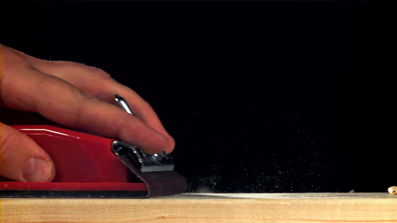 Close-up van een hand die hout schuurt met een rood schuurblok