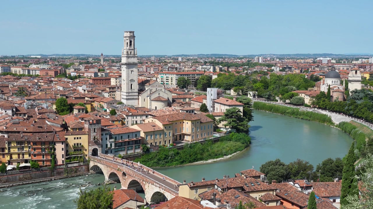 Vista panorâmica de Verona, Itália, apresentando a Ponte Pietra, o Rio Adige e o horizonte histórico da cidade, de um ponto de vista elevado em um dia ensolarado.