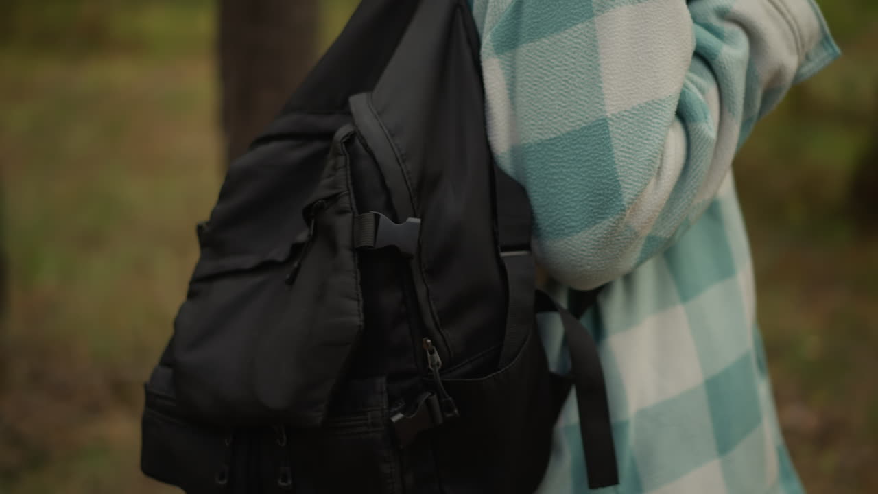 Una persona regola gli spallacci all'aperto, un individuo modifica la cinghia dello zaino in un paesaggio autunnale, un appassionato di attività all'aperto personalizza la cinghia dello zaino immerso nella tranquillità di un bosco autunnale