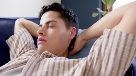 Tired-biracial-man-lying-on-couch-resting-with-eyes-closed,-slow-motion