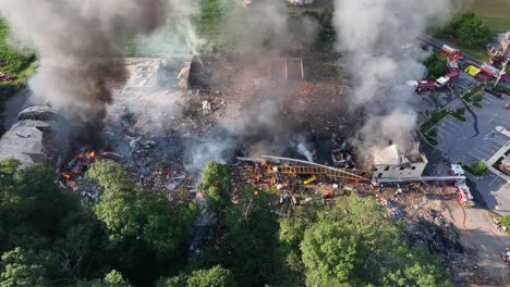 Aerial-downward-angle-of-firemen-spraying-water-on-gas-explosion-aftermath,-usa