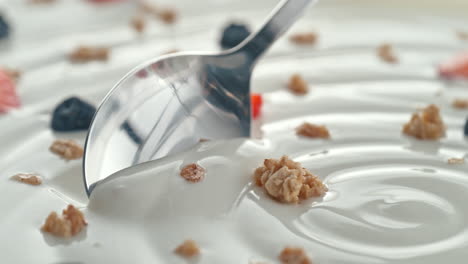 muesli with fruit scooped with silver spoon from creamy thick yogurt in macro and slow motion