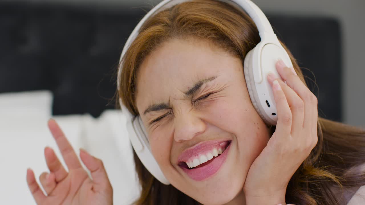 Donna afroamericana che reagisce a una canzone, tiene le cuffie bianche, canta e ride sul letto.