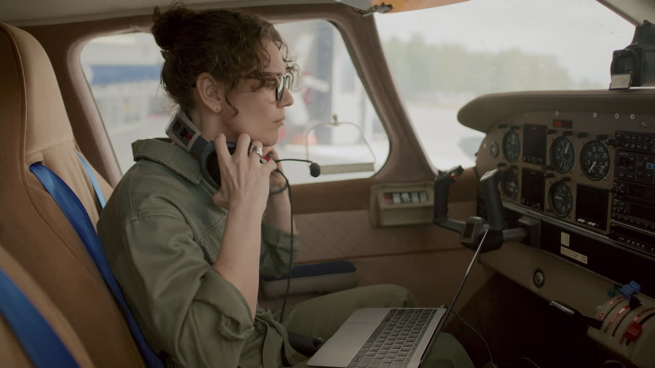Female Pilot Using Laptop and Talking on Headset with Mic inside Cockpit