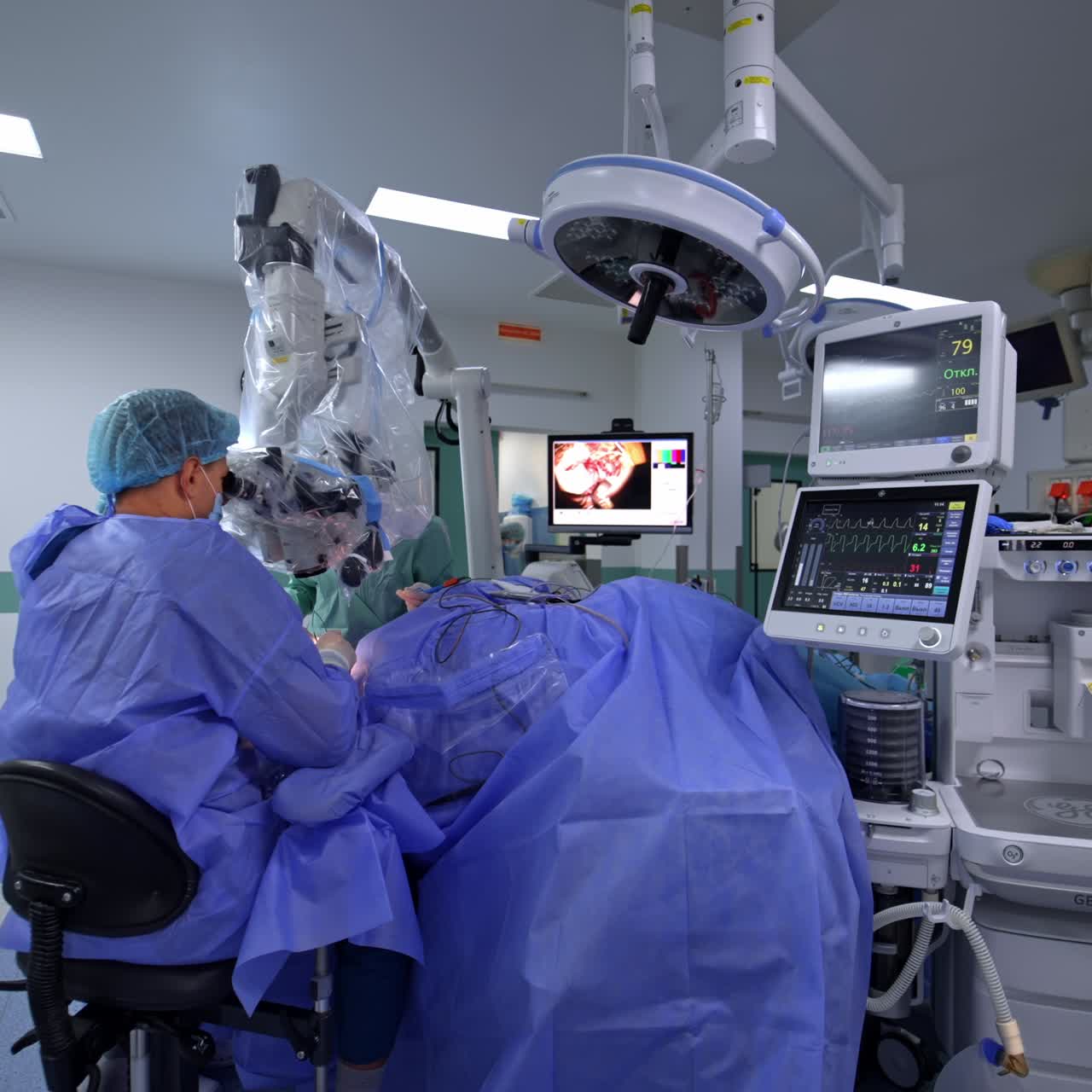Male neurosurgeon sitting at the patient and operating him looking at high-tech microscope. Advanced equipment working at surgery room at backdrop