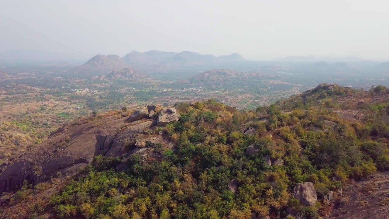 Aerial drone view of a small water body beyond Ramanagara Hills with arid land and vegetation in Karnataka, India.