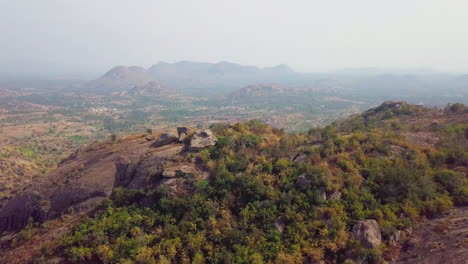 aerial drone view of a small water body beyond ramanagara hills with arid land and vegetation in karnataka, india.