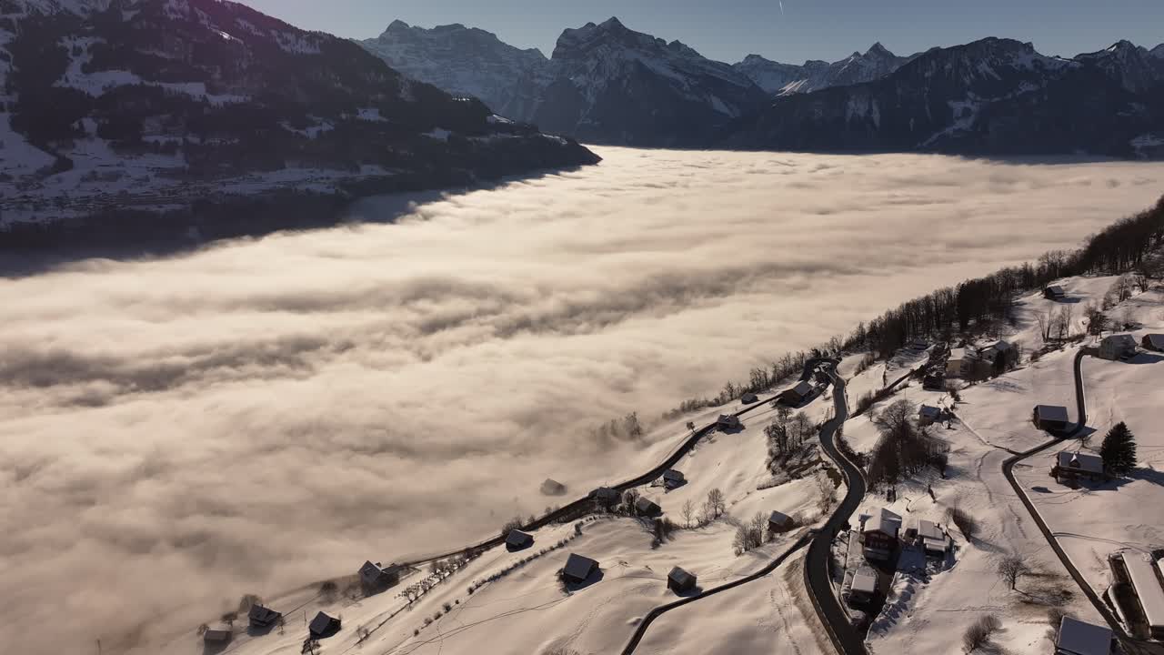 A breathtaking aerial view of snow-covered mountains and misty valleys, capturing the beauty of Switzerland's Walensee area, with the villages of Amden and Weesen.