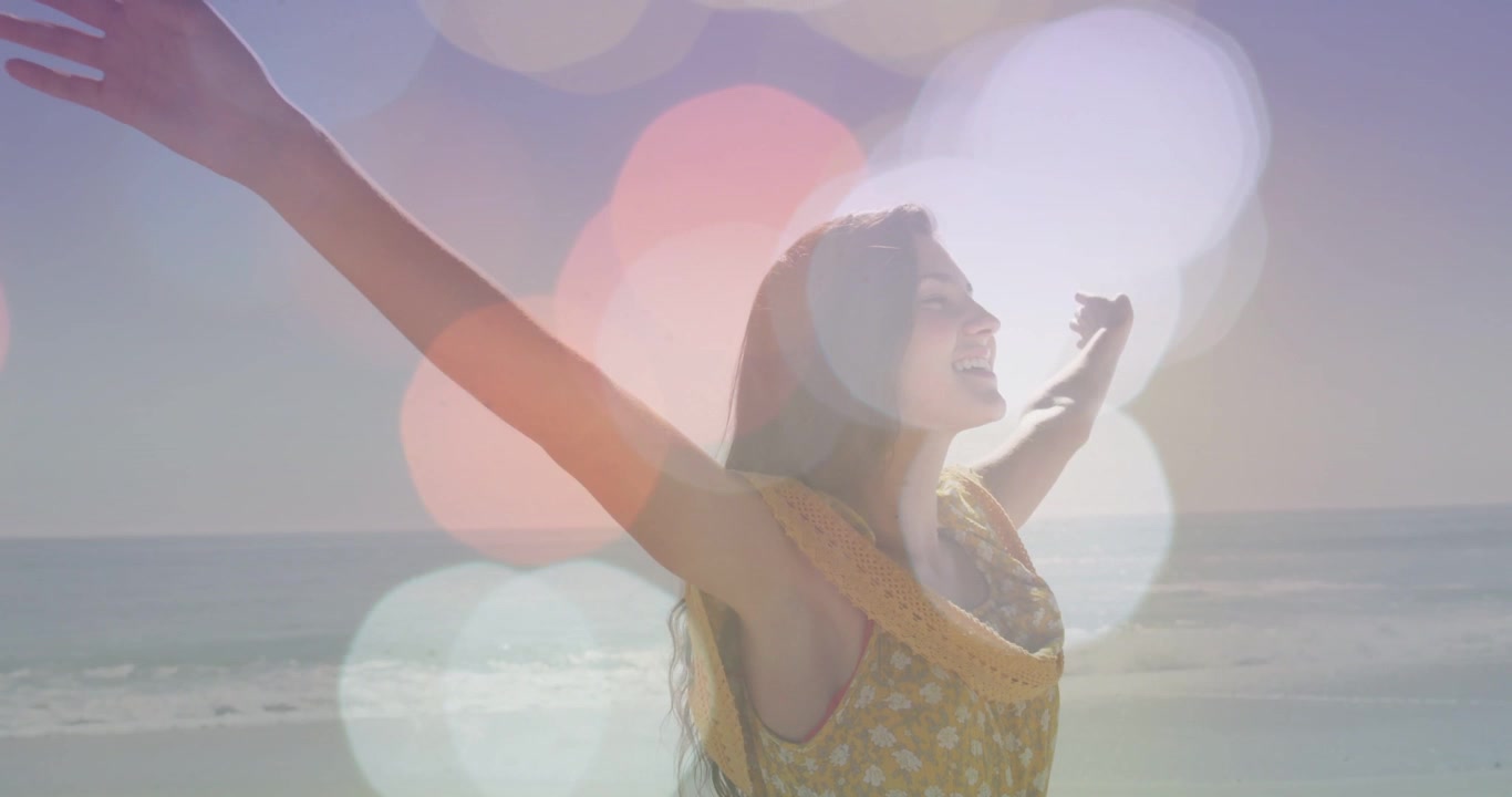 Sunlight causing woman in yellow dress opening arms at sandy shore, waves, bokeh, copy space