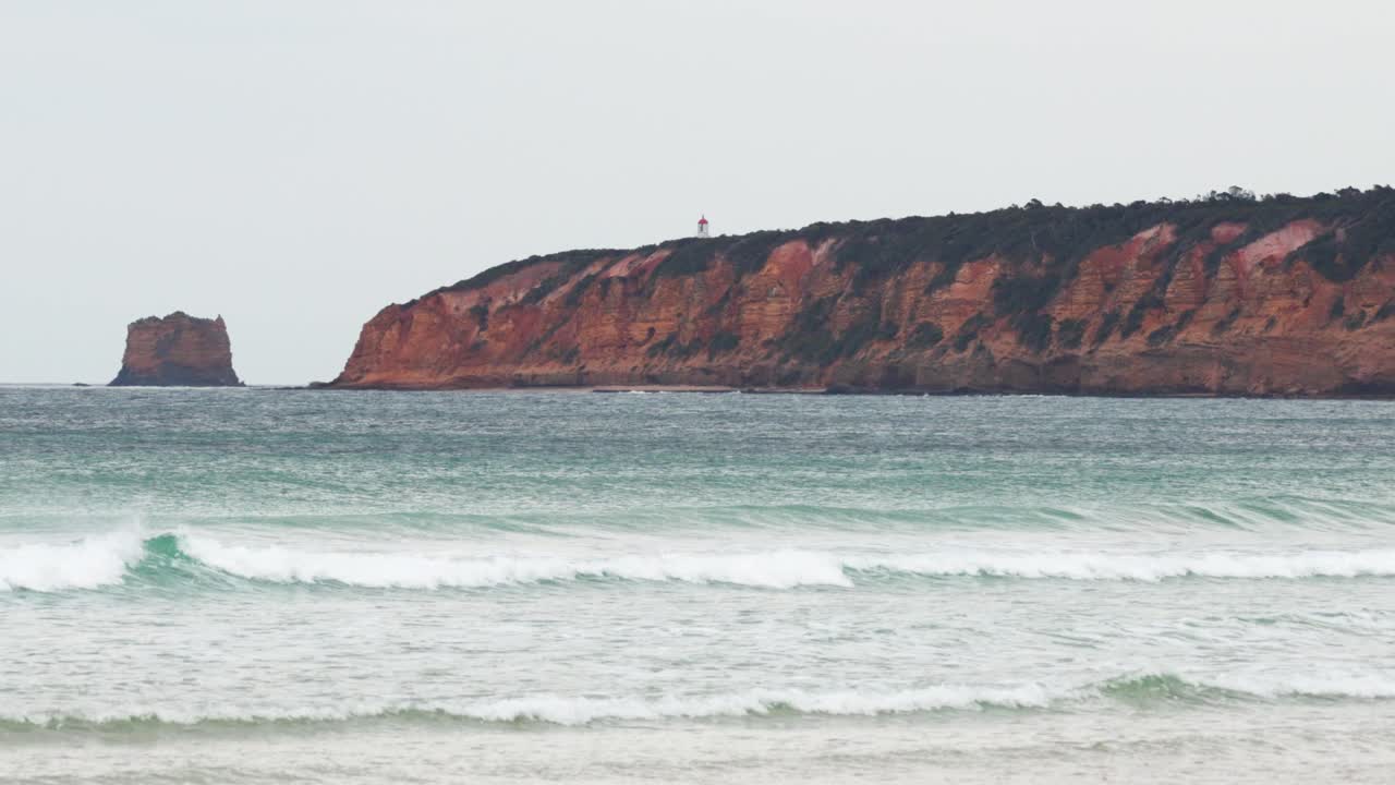 A serene view of waves rolling onto the shore with a rocky coastline backdrop, captured along the Great Ocean Road