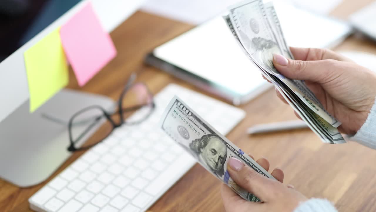 A person counting hundred dollar bills at a desk