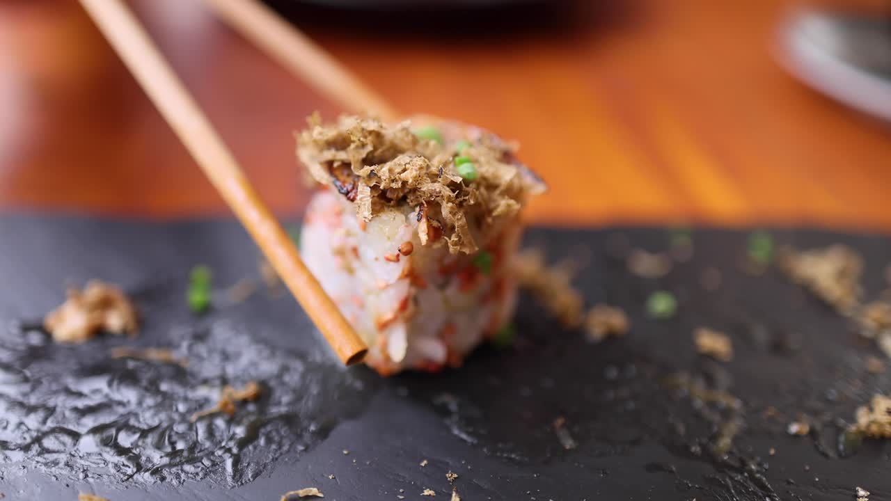 Hůlky uchopující sushi rolku z talíře.