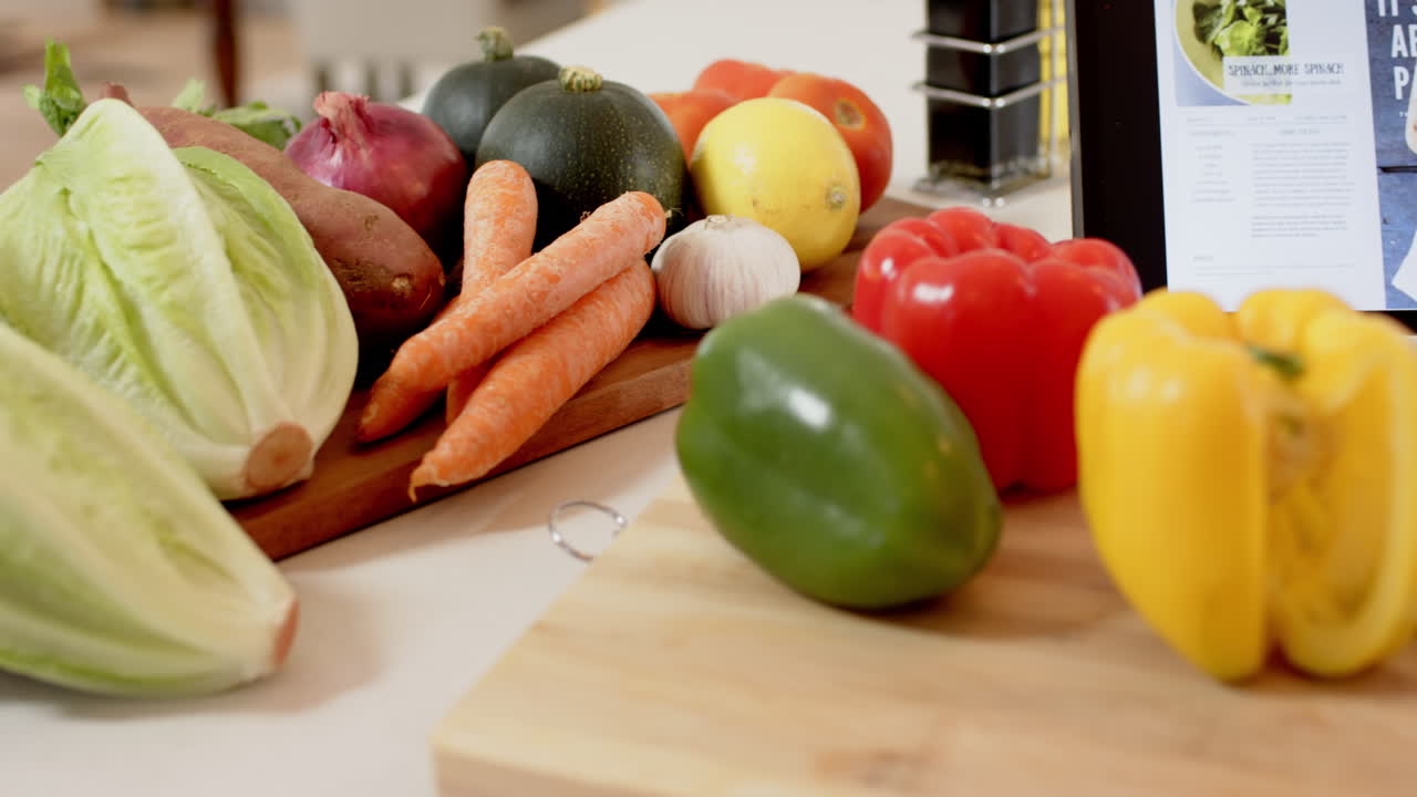 Fresh vegetables on cutting board with tablet displaying recipe for cooking