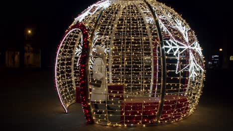 woman in a white jacket and hat walking inside a giant christmas tree bauble and cheering