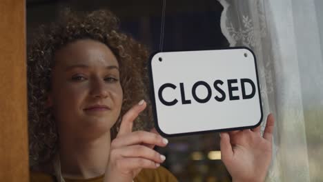 caucasian waitress changing sign on doors from closed to open.