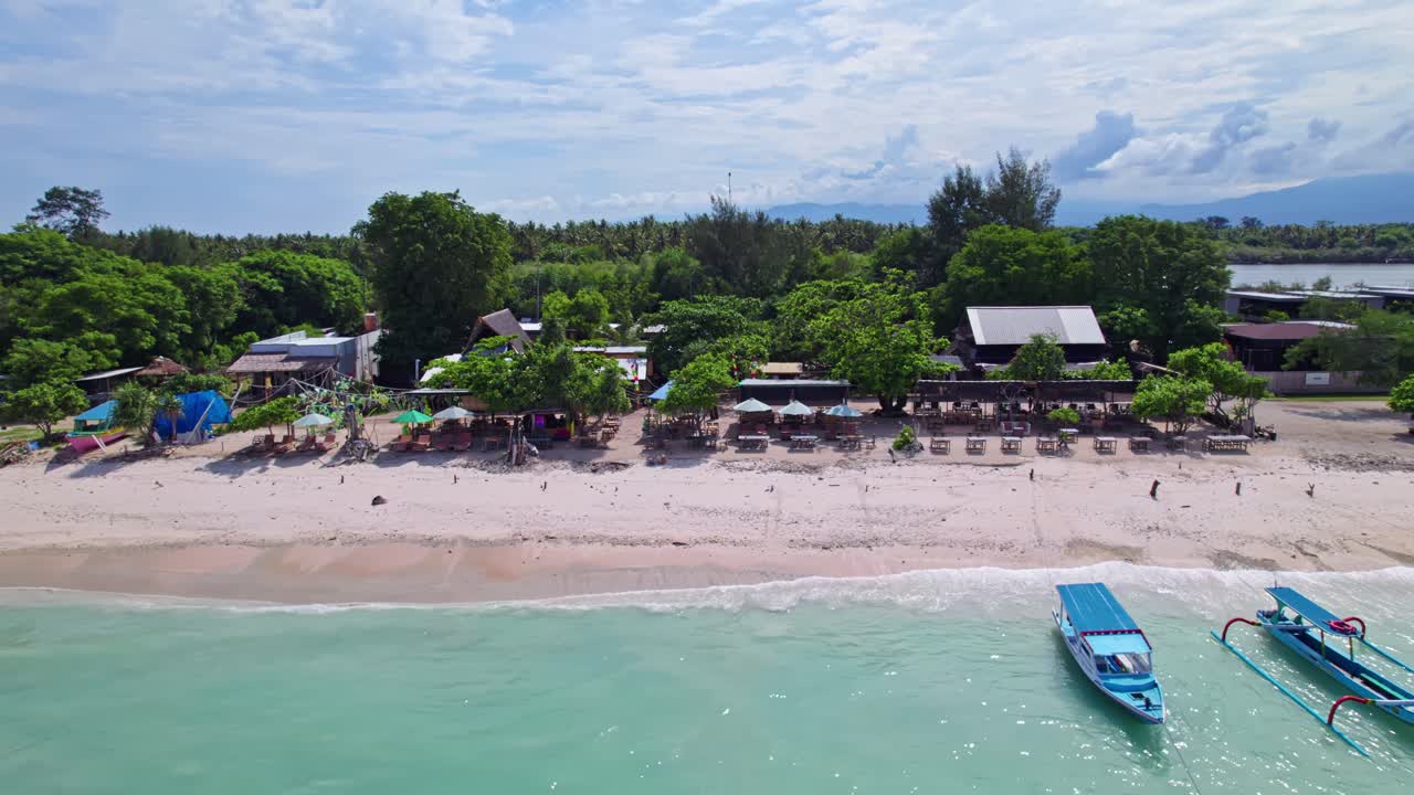 Restaurants and boats along Gili Meno Island beach, low aerial tracking sideways