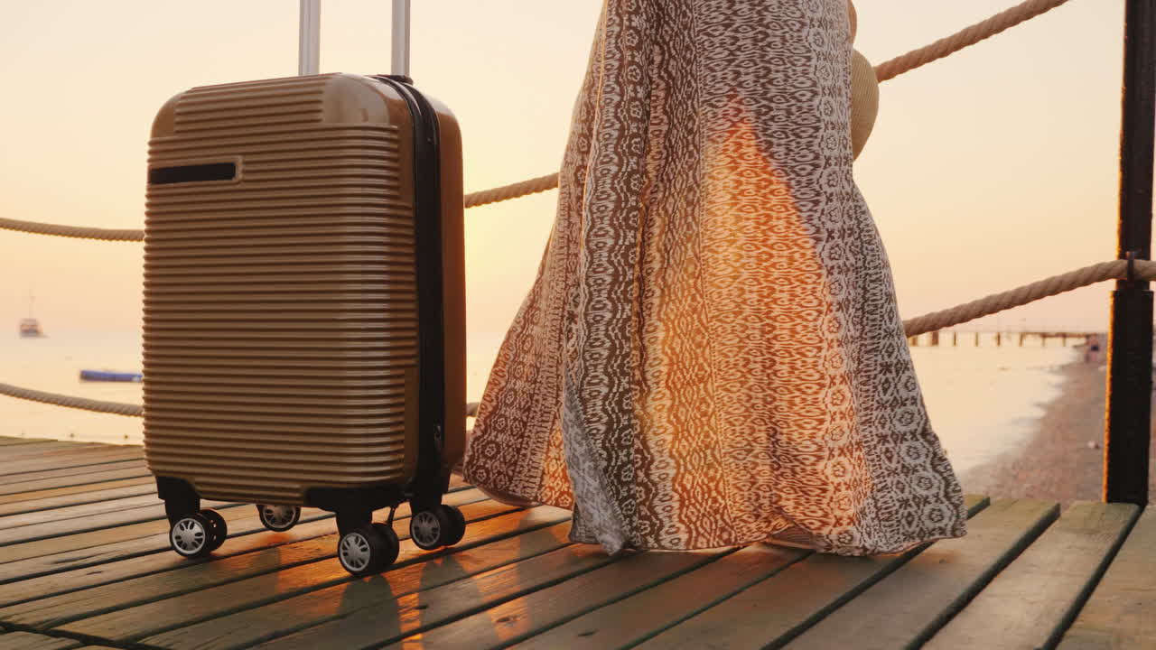 Om de rust te vinden: een koffer op wielen met een meisje in een zwierige jurk op een pier aan de zeekust.