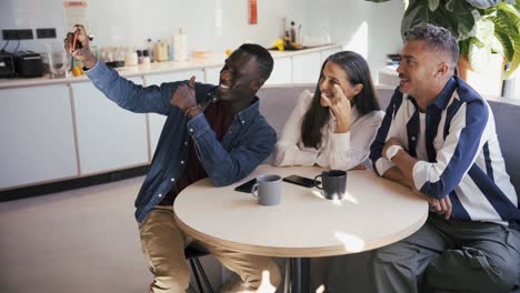 Cheerful-multiethnic-colleagues-taking-a-selfie-with-smartphone-in-cafe