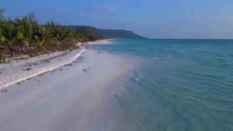 a pristine beach with palm trees meeting the crystal clear turquoise water on koh rong island, cambodia. great aerial view flight fly reverse drone