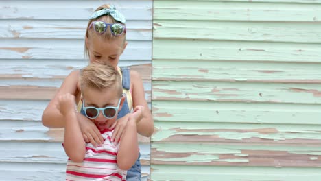 Portrait-of-happy-caucasian-siblings-with-sunglasses-raising-hands-over-beach-house