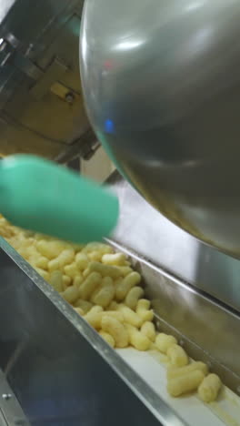 pouring corn sticks of snacks from a metal tank onto an automatic conveyor belt. hand of a worker with a shovel. food factory. vertical video