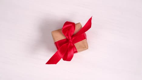 gift box with red ribbon spinning on pink wood background. 360 degree rotation. seamless loop. concept sales, discount price, christmas holidays and shopping