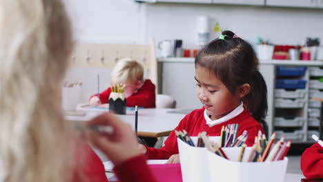 escolar china sentada en la mesa dibujando y hablando con sus compañeros de clase de la escuela infantil, de cerca