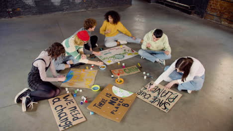 top view of young environmental activists painting placards sitting on the floor