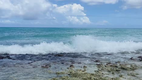 Olas-Rompiendo-Suavemente-En-Una-Orilla-Rocosa-Bajo-Un-Cielo-Azul-Claro-Con-Nubes-Blancas-Esponjosas