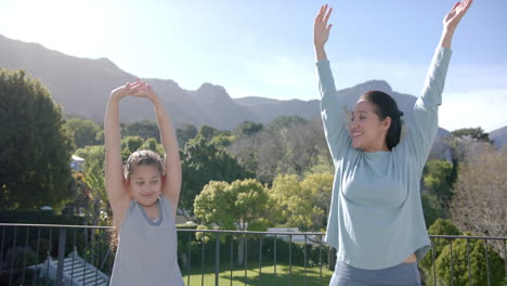 happy biracial mother and daughter practising yoga on terrace in sunny day, slow motion