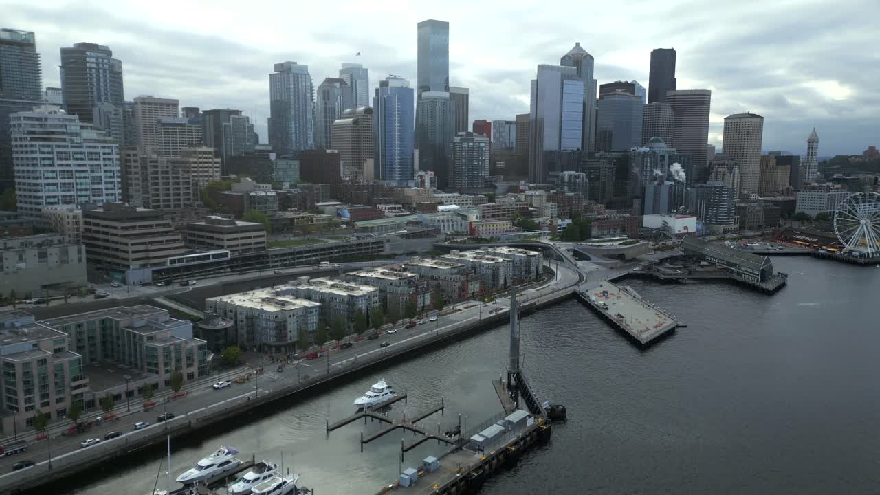 Scenic flyover shot of downtown Seattle city buildings and streets facing calm coastline along Seattle Waterfront, Washington, USA.