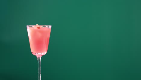 a pink cocktail in a glass on a green screen background. steady camera, vibrant colors, and minimalistic composition