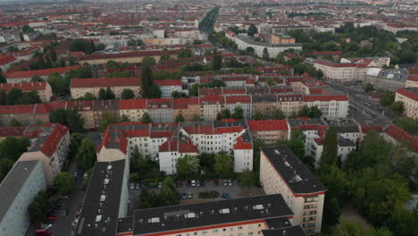 Forwards-fly-above-buildings-in-urban-neighbourhood.-Tilt-up-reveal-of-large-city-with-long-straight-street-and-Fernsehturm-TV-tower-in-distance.-Berlin,-Germany