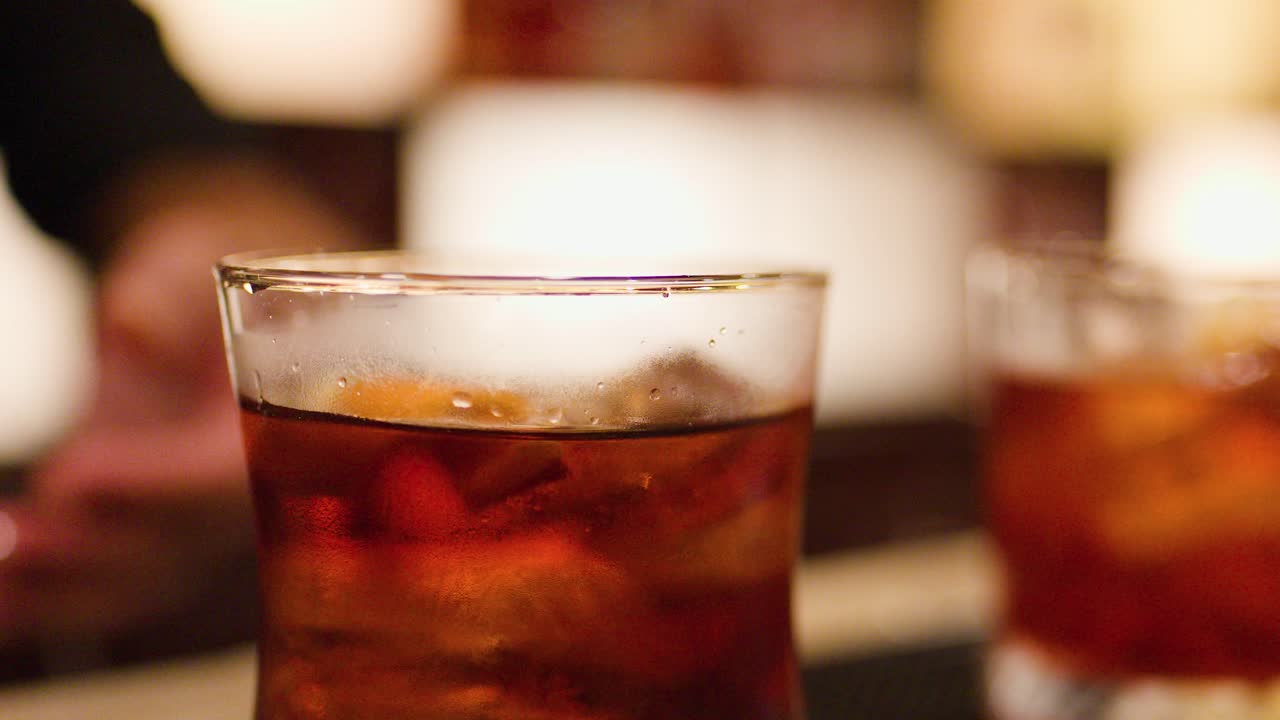 Hand adds orange peel to whiskey cocktail in dimly lit bar, close-up, shallow focus