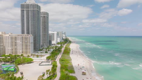Amazing-aerial-view-of-ocean-coast.-Mild-waves-washing-sand-beach-lined-by-apartment-buildings-and-hotels.-Miami,-USA