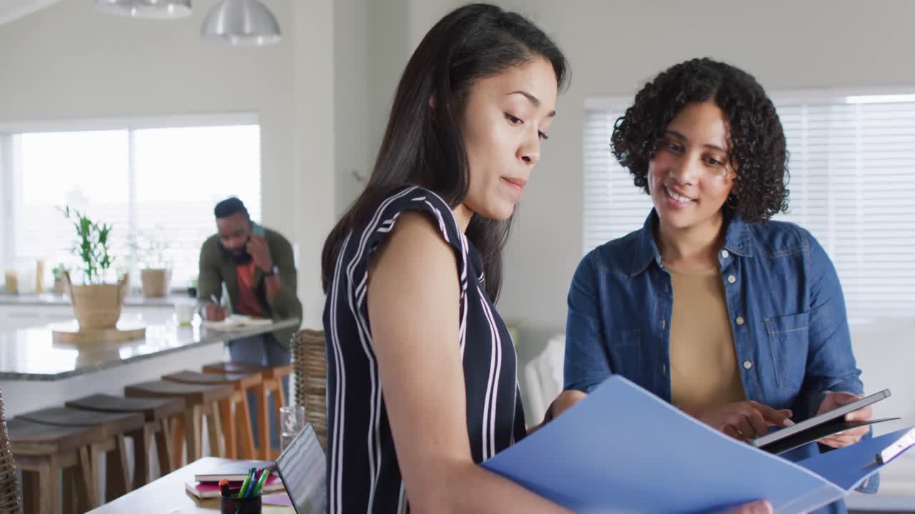 amigas felices y diversas hablando y sosteniendo archivos, trabajando en casa, en cámara lenta.