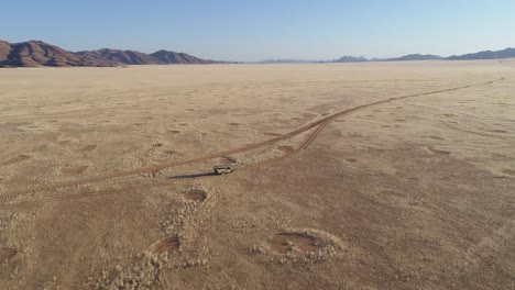 4k high tilt up aerial view of a 4x4 safari vehicle driving on a sand track through the african savannah grasslands with the famous fairy circles, namibia