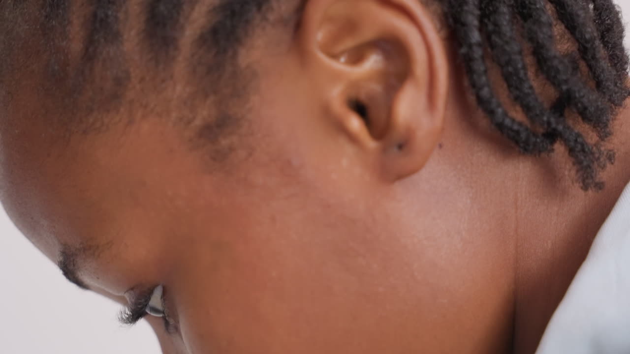 Giovane ragazza che guarda in basso, studio ravvicinato. Profilo intimo di una bambina con i capelli a trecce che si concentra sulla lettura o sui compiti in un interno tranquillo, con uno sfondo minimale. Sguardo concentrato, ombre morbide, scena quotidiana.