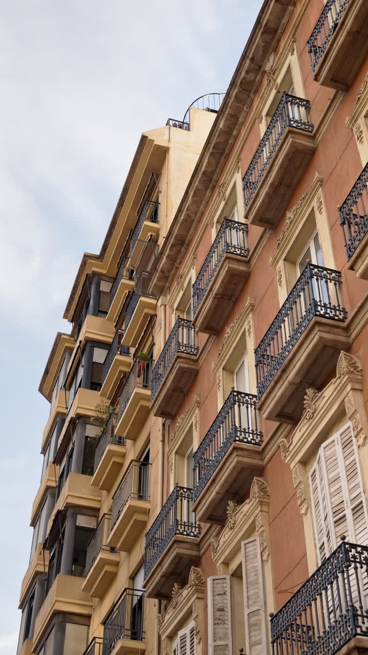 Vista dal basso angolo di edifici residenziali tradizionali ad Alicante, in Spagna, caratterizzati da facciate decorate, balconi in ferro battuto e finestre con persiane. Verticale
