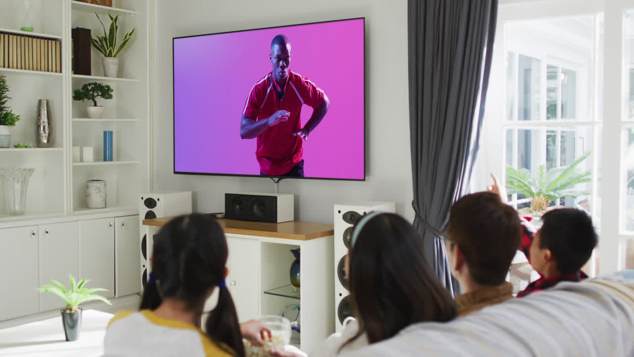 Asian family watching tv with african american male rugby player catching ball on screen