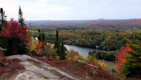 Standing-on-top-of-a-rock-bolder-high-on-a-mountain-looking-down-at-a-large-lake-during-the-day